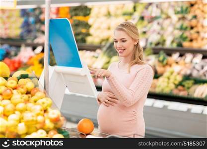 sale, shopping, food, pregnancy and people concept - happy pregnant woman weighing grapefruit on scale at grocery store or supermarket. pregnant woman with grapefruit on scale at grocery