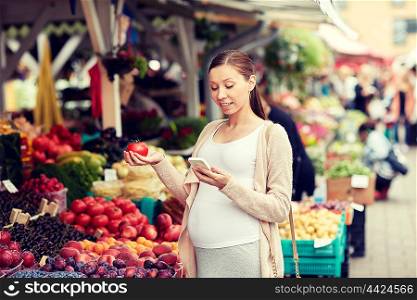 sale, shopping, food, pregnancy and people concept - happy pregnant woman with smartphone choosing vegetables at street market