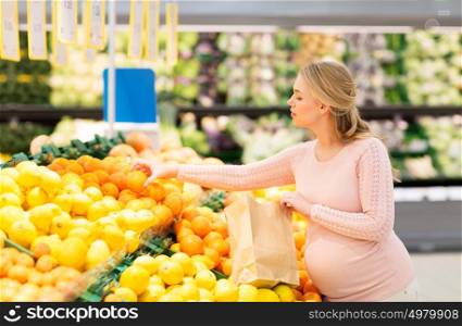 sale, shopping, food, pregnancy and people concept - happy pregnant woman with paper bag buying oranges at grocery store or supermarket. pregnant woman with bag buying oranges at grocery