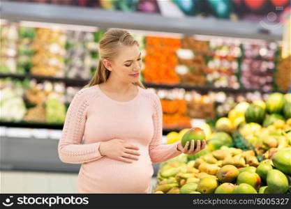 sale, shopping, food, pregnancy and people concept - happy pregnant woman with mango at grocery store or supermarket. happy pregnant woman with mango at grocery store