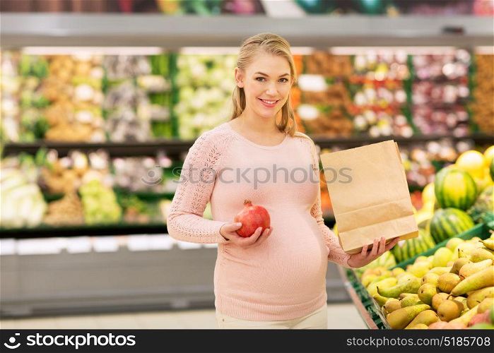 sale, shopping, food, pregnancy and people concept - happy pregnant woman with paper bag buying pomegranates at grocery store or supermarket. pregnant woman with bag buying fruits at grocery