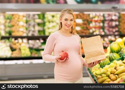 sale, shopping, food, pregnancy and people concept - happy pregnant woman with paper bag buying pomegranates at grocery store or supermarket. pregnant woman with bag buying fruits at grocery
