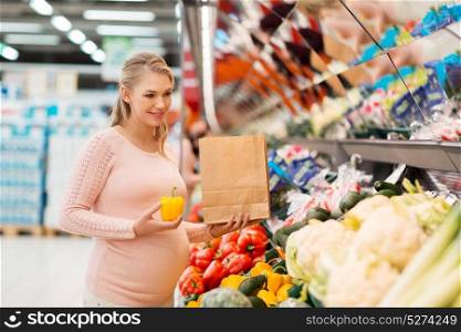 sale, shopping, food, pregnancy and people concept - happy pregnant woman with paper bag buying peppers at grocery store or supermarket. pregnant woman buying vegetables at grocery store