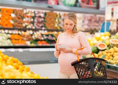 sale, shopping, food, pregnancy and people concept - happy pregnant woman with basket and notebook at grocery store or supermarket. pregnant woman with shopping basket at grocery