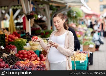 sale, shopping, food, pregnancy and people concept - happy pregnant woman with smartphone choosing vegetables at street market