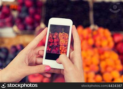 sale, shopping, food, technology and people concept - close up of hands with smartphone taking picture of fruits at street market