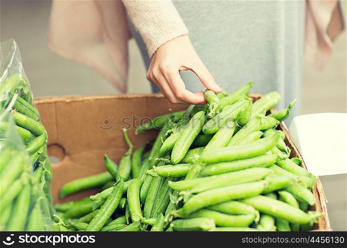 sale, shopping, food, vegetables and people concept - close up of woman hand choosing green peas at street market