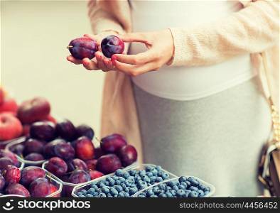 sale, shopping, pregnancy and people concept - close up of pregnant woman choosing plums at street food market