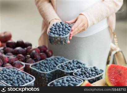 sale, shopping, pregnancy and people concept - close up of pregnant woman choosing blueberries at street food market