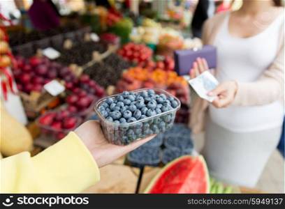 sale, shopping, pregnancy and people concept - close up of pregnant woman with wallet and money buying blueberry at street food market