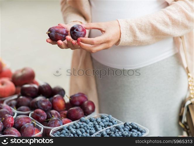 sale, shopping, pregnancy and people concept - close up of pregnant woman choosing plums at street food market