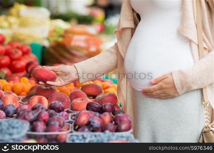 sale, shopping, pregnancy and people concept - close up of pregnant woman choosing saturn peaches at street food market