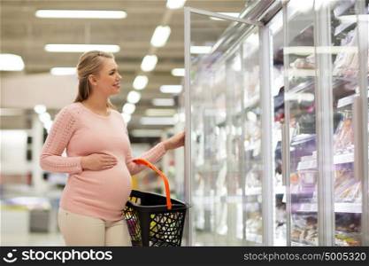 sale, shopping, pregnancy and people concept - happy pregnant woman with basket at grocery store or supermarket fridge. pregnant woman with shopping basket at store