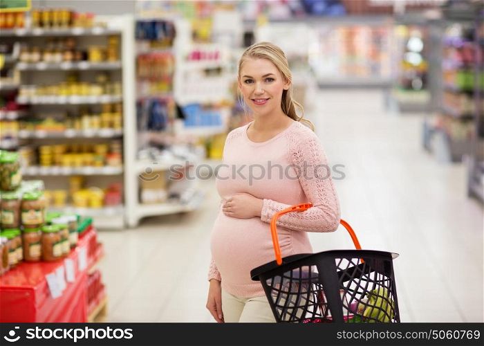 sale, shopping, pregnancy and people concept - happy pregnant woman with basket at grocery store or supermarket. pregnant woman with shopping basket at grocery