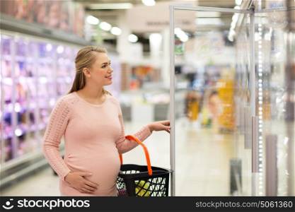 sale, shopping, pregnancy and people concept - happy pregnant woman with basket at grocery store or supermarket fridge. pregnant woman with shopping basket at store