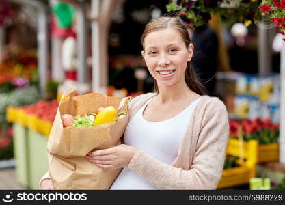 sale, shopping, pregnancy and people concept - happy pregnant woman with paper bag full of food at street market