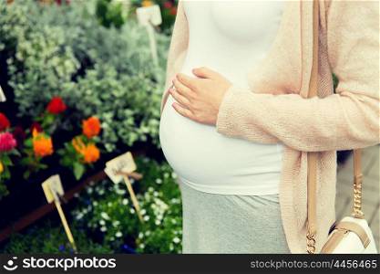 sale, shopping, pregnancy, gardening and people concept - close up of pregnant woman choosing flowers and touching her tummy at street market