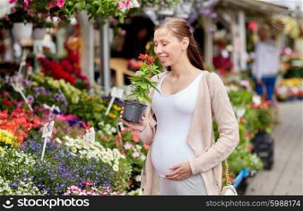 sale, shopping, pregnancy, gardening and people concept - happy pregnant woman choosing and smelling flowers at street market