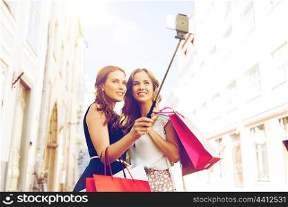 sale, technology, friendship and people concept - happy young women with shopping bags taking picture by smartphone selfie stick on city street