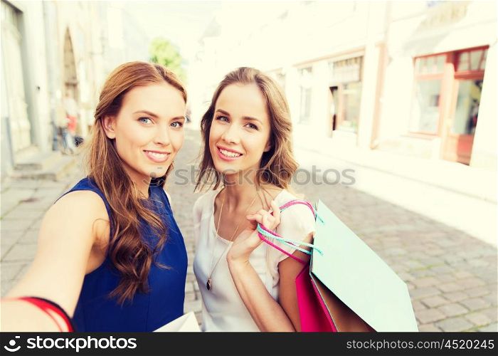 sale, technology, friendship and people concept - happy young women with shopping bags taking selfie by smartphone on city street