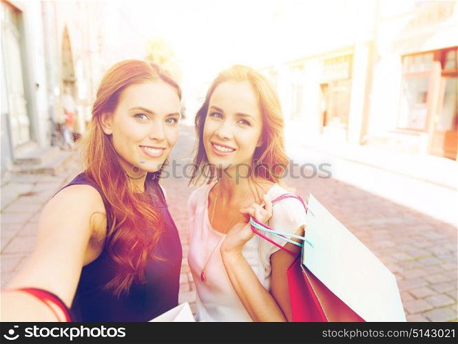 sale, technology, friendship and people concept - happy young women with shopping bags taking selfie by smartphone on city street. women shopping and taking selfie by smartphone
