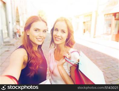 sale, technology, friendship and people concept - happy young women with shopping bags taking selfie by smartphone on city street. women shopping and taking selfie by smartphone