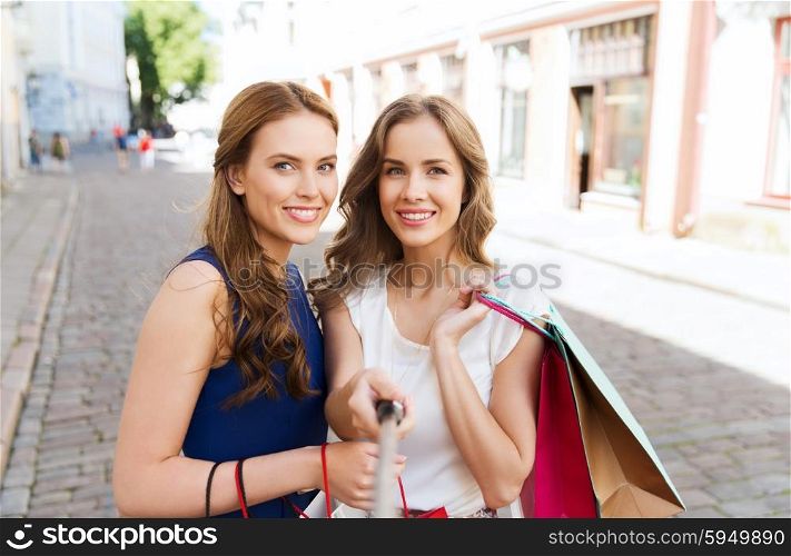 sale, technology, friendship and people concept - happy young women with shopping bags taking picture by smartphone selfie stick on city street
