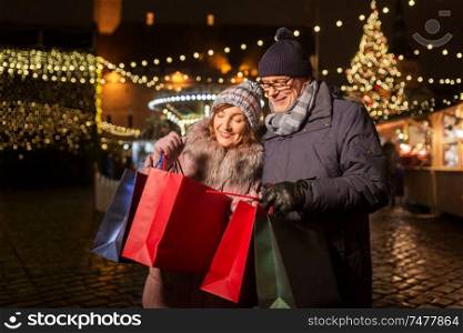 sale, winter holidays and people concept - happy senior couple with shopping bags at christmas market souvenir shop on town hall square in tallinn, estonia. old couple at christmas market with shopping bags