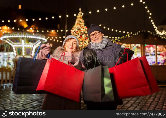 sale, winter holidays and people concept - happy senior couple with shopping bags at christmas market souvenir shop on town hall square in tallinn, estonia. old couple at christmas market with shopping bags