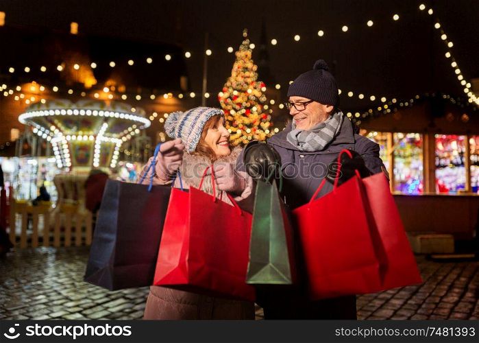 sale, winter holidays and people concept - happy senior couple with shopping bags at christmas market souvenir shop on town hall square in tallinn, estonia. old couple at christmas market with shopping bags