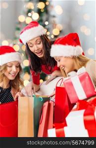 sale, winter holidays and people concept - smiling young woman in santa helper hat with gifts and shopping bags over christmas tree lights background