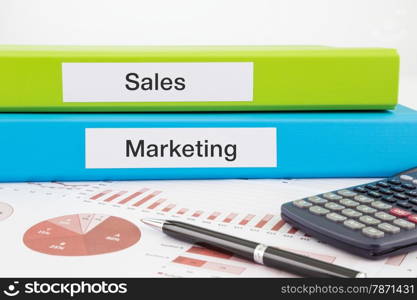 Sales and Marketing words on labels with document binders, graphs and business reports