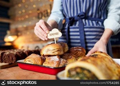 Sales Assistant In Bakery Putting Homemade Label Into Stack Of Freshly Baked Baked Cinnamon Buns