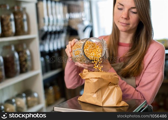 Sales Assistant In Sustainable Plastic Free Grocery Store Weighing Corn Into Paper Bag