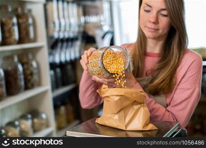 Sales Assistant In Sustainable Plastic Free Grocery Store Weighing Corn Into Paper Bag