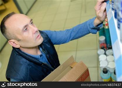 sales assistant shelving spray cans at hardware store