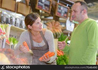 Sales assistant with customer, holding carrots