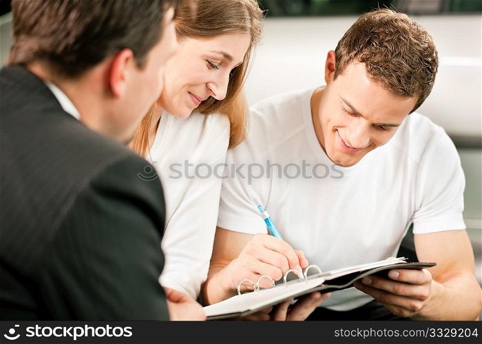 Sales situation in a car dealership, the young couple is signing the sales contract to get the new car in the background