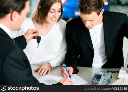 Sales situation in a car dealership, the young couple is signing the sales contract and gets the key for the new car