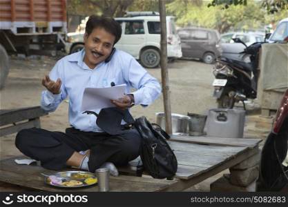 Salesman talking on a mobile phone and smiling holding papers