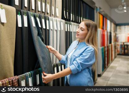 Saleswoman measures fabric in textile store. Shelf with cloth for sewing on background, clothing patterns choice in shop. Saleswoman measures fabric in textile store