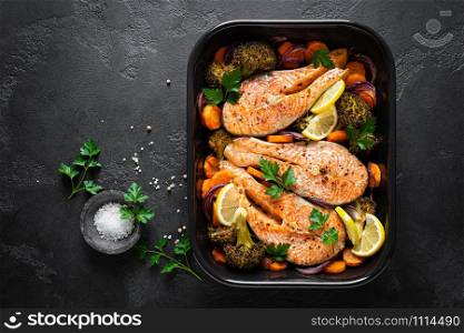 Salmon. Baked salmon fish steaks with vegetables, broccoli, carrot and onion on black background, top view