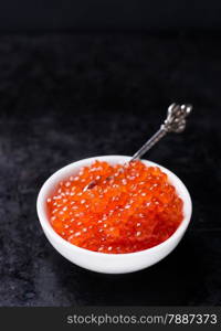 Salmon caviar in white bowl on dark background, selective focus