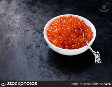 Salmon caviar in white bowl on dark background, selective focus