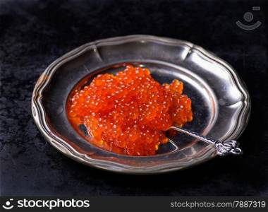 Salmon caviar on metal plate on dark background, selective focus