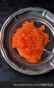 Salmon caviar on metal plate on dark background, selective focus