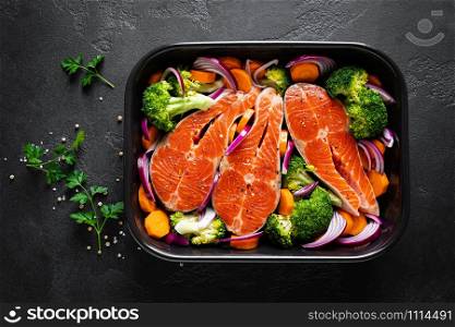 Salmon. Cooking fresh raw salmon fish steaks with vegetables, broccoli, carrot and onion on black background, top view