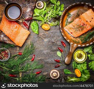 Salmon fillet on rustic kitchen table with fresh ingredients for tasty cooking and frying pan. Wooden background, frame, top view. Healthy and diet food concept.