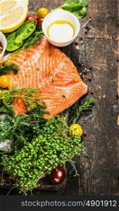 Salmon fillet with oil and fresh ingredients for cooking on rustic wooden background, top view, place for text
