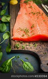 Salmon fillets on cutting board and fresh ingredients for cooking, close up